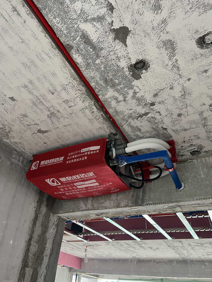 吊在混凝土頂板下的中央空調室內機，機身掛紅色風口標識布，下方已架起木質吊頂龍骨架，側面盤繞白色波紋管與藍色保溫管